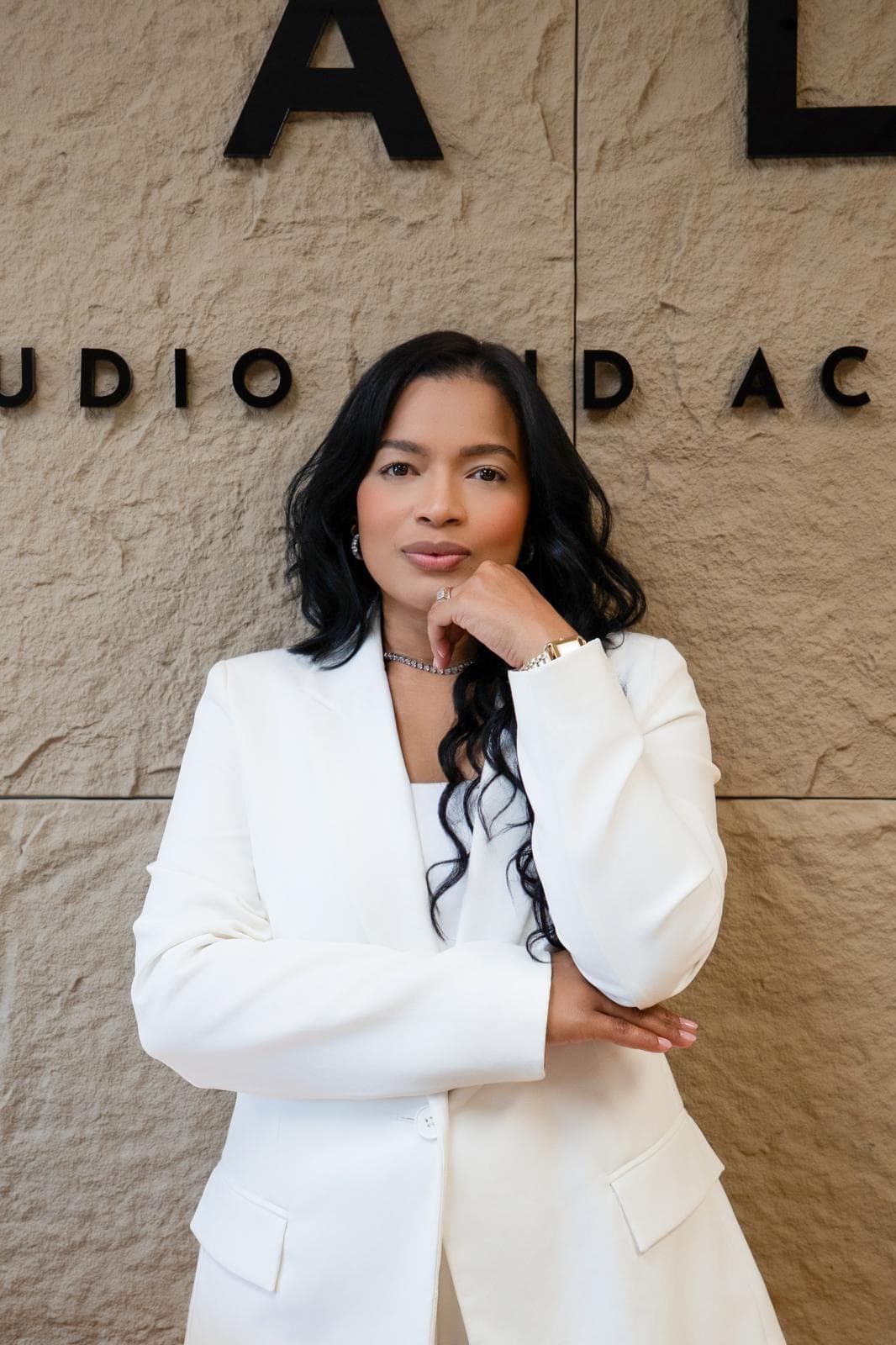 Yeimi Arellano, founder of Cala Studio, in a white suit, in front of the studio’s stone wall and sign