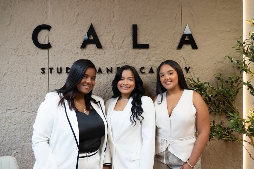 Valeria, Yeimi and Yamilka in white in front of the CALA Studio and Academy sign