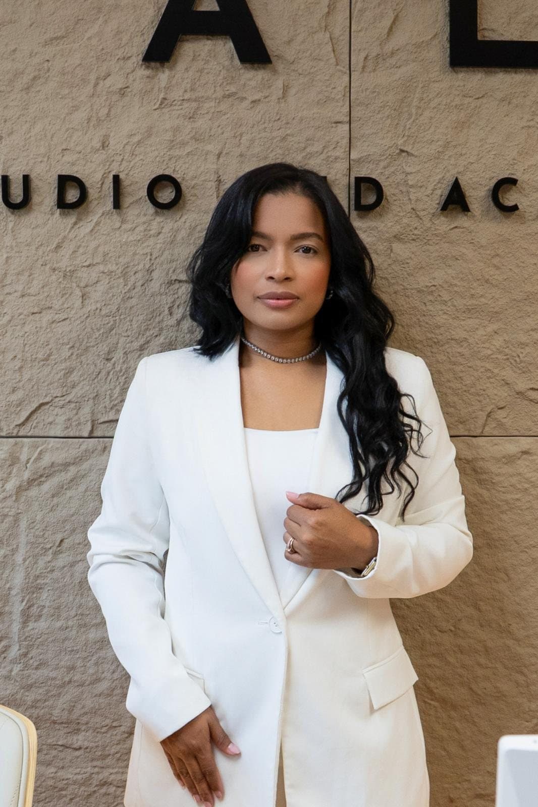 Yeimi Arellano, founder of Cala Studio, in a white suit, in front of the studio’s stone wall and sign